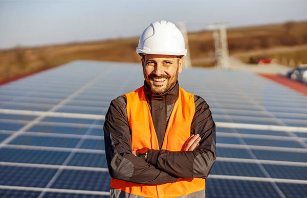 Engineer in a hard hat and safety vest standing confidently in front of solar panels