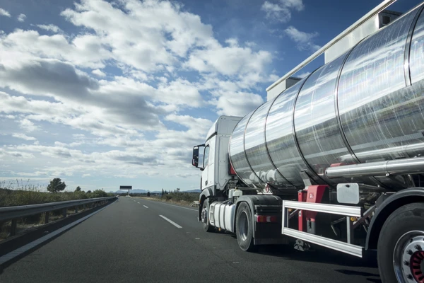 Shiny stainless steel tanker truck driving on a highway under a partly cloudy sky