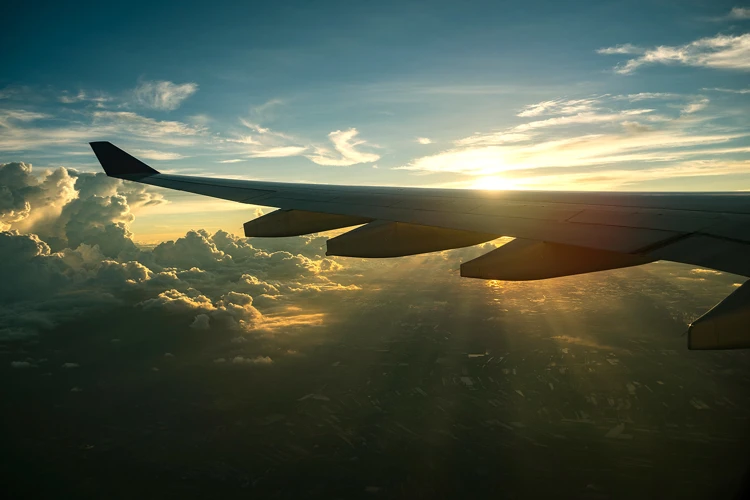 View of an airplane wing during flight at sunset, with golden sunlight illuminating clouds and the landscape below.